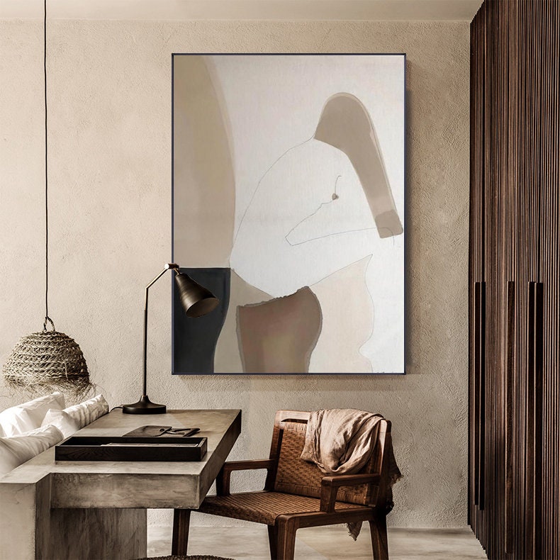 May include: Abstract painting of a person in a seated pose, with muted tones of brown, beige, and white. The painting is framed and hanging on a wall in a modern interior.