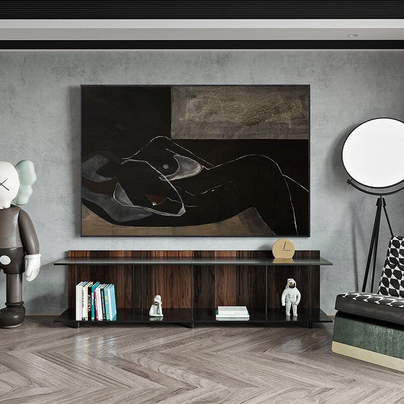 May include: A black and white abstract painting of a nude figure lying down on a bed. The painting is framed and hanging on a gray wall above a dark wood shelf with books and figurines.