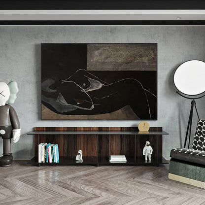 May include: A black and white abstract painting of a nude figure lying down on a bed. The painting is framed and hanging on a gray wall above a dark wood shelf with books and figurines.