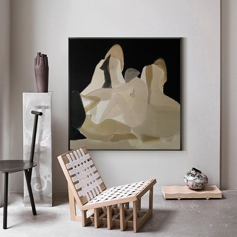 May include: Abstract painting of three figures in shades of beige and brown on a black background. The painting is framed in black and hangs on a white wall.