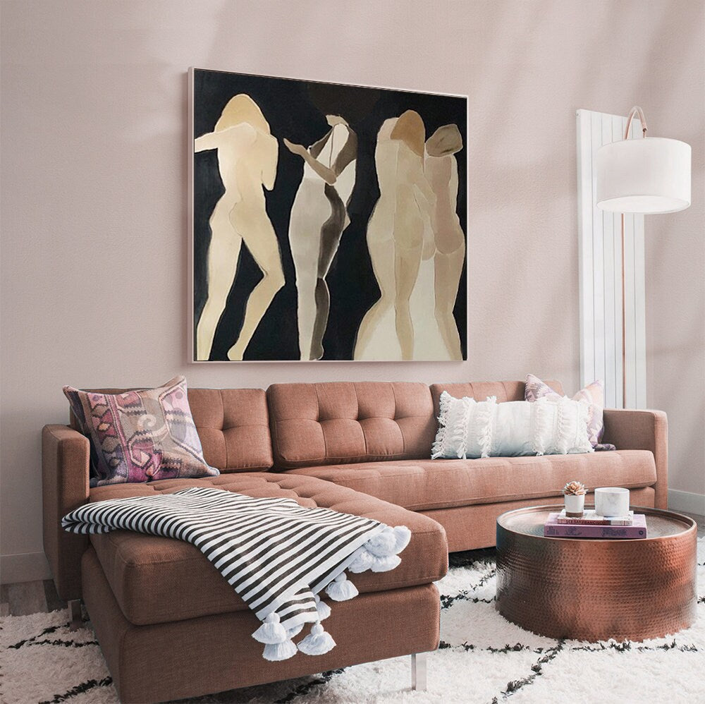 May include: A brown sectional sofa with a white and black striped throw blanket and a copper coffee table. The sofa is in front of a pink wall with a painting of three abstract figures in shades of brown and beige.