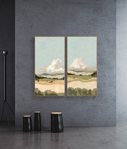 May include: Two framed landscape paintings with a light blue sky, white clouds, and green and brown hills. The paintings are hanging on a gray wall.