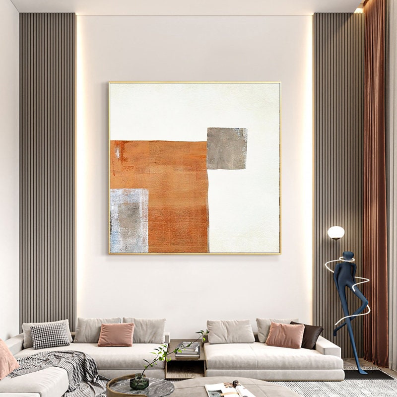 May include: Abstract painting with geometric shapes in shades of brown, gray, and white. The painting is framed in a gold frame and hangs on a white wall.