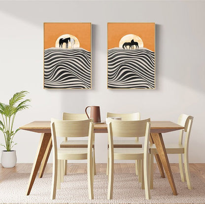May include: Two abstract art prints with black silhouettes of horses on a white and black striped background with an orange sun in the background. The prints are hanging on a white wall above a wooden dining table with four light wood chairs.