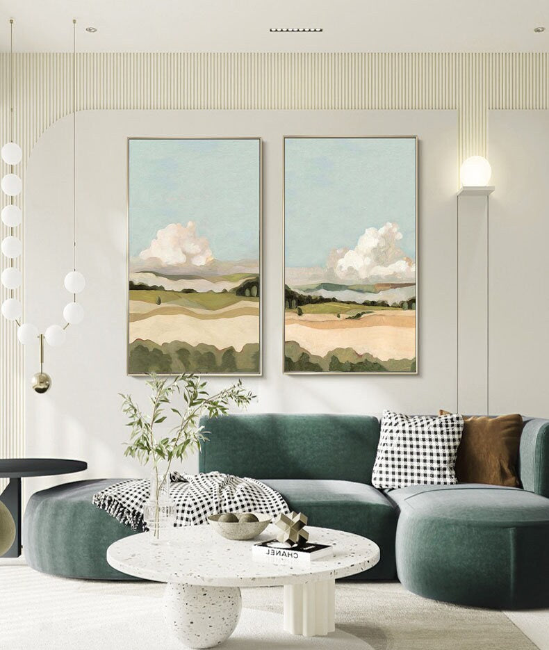 May include: Two framed landscape paintings with a green, brown, and blue color scheme. The paintings depict a field with rolling hills and fluffy white clouds in the sky.