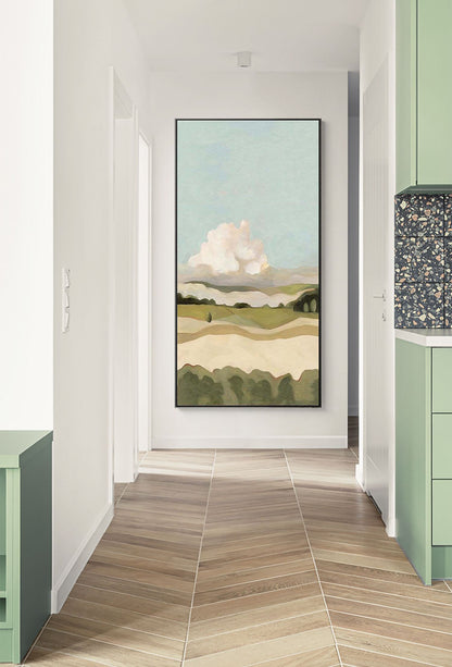May include: A framed abstract landscape painting with a large white cloud in a blue sky over rolling green hills. The painting is in a black frame and is hanging on a white wall in a hallway.
