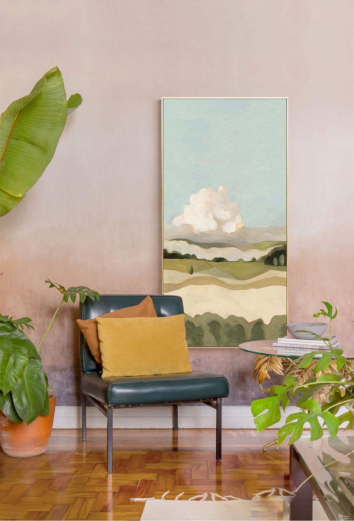May include: A green armchair with two yellow throw pillows sits in front of a painting of a landscape with a large white cloud in the sky. The painting is framed in gold and hangs on a light pink wall.
