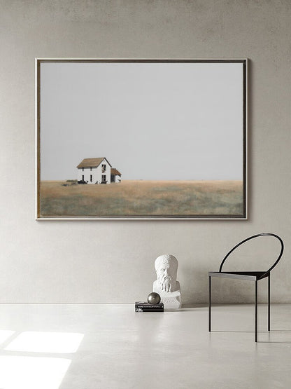 May include: A framed photograph of a white farmhouse with a brown roof in a field. The farmhouse is in the distance and the sky is a light gray. The photograph is hanging on a white wall.