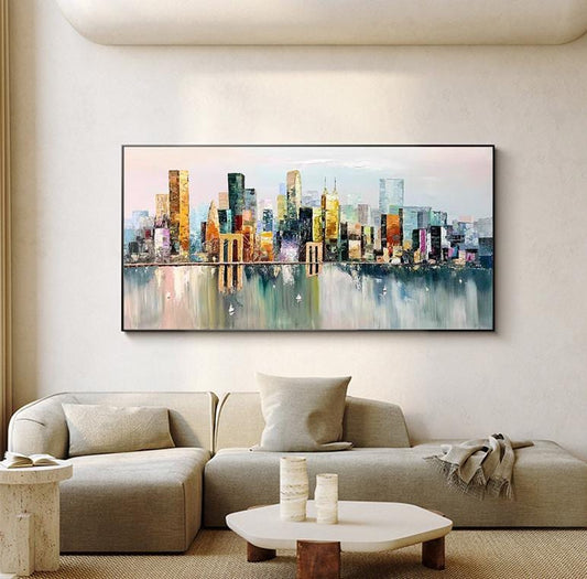 May include: Abstract painting of a cityscape with colorful buildings reflected in a body of water. The painting is framed and hanging on a wall in a room with a couch and coffee table.