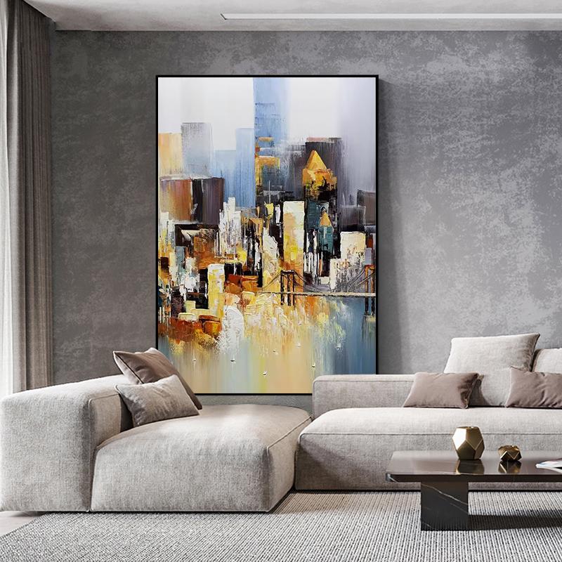 May include: Abstract painting of a cityscape in shades of brown, yellow, and blue. The painting depicts a city skyline with tall buildings and a bridge. The painting is framed in a black frame and is hanging on a gray wall.