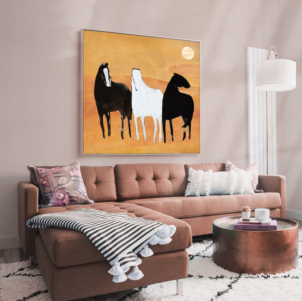 May include: Abstract painting of three horses in black, white, and gray against a yellow background. The horses are standing side by side, with their heads turned in different directions. The painting is framed and hanging on a wall in a living room.