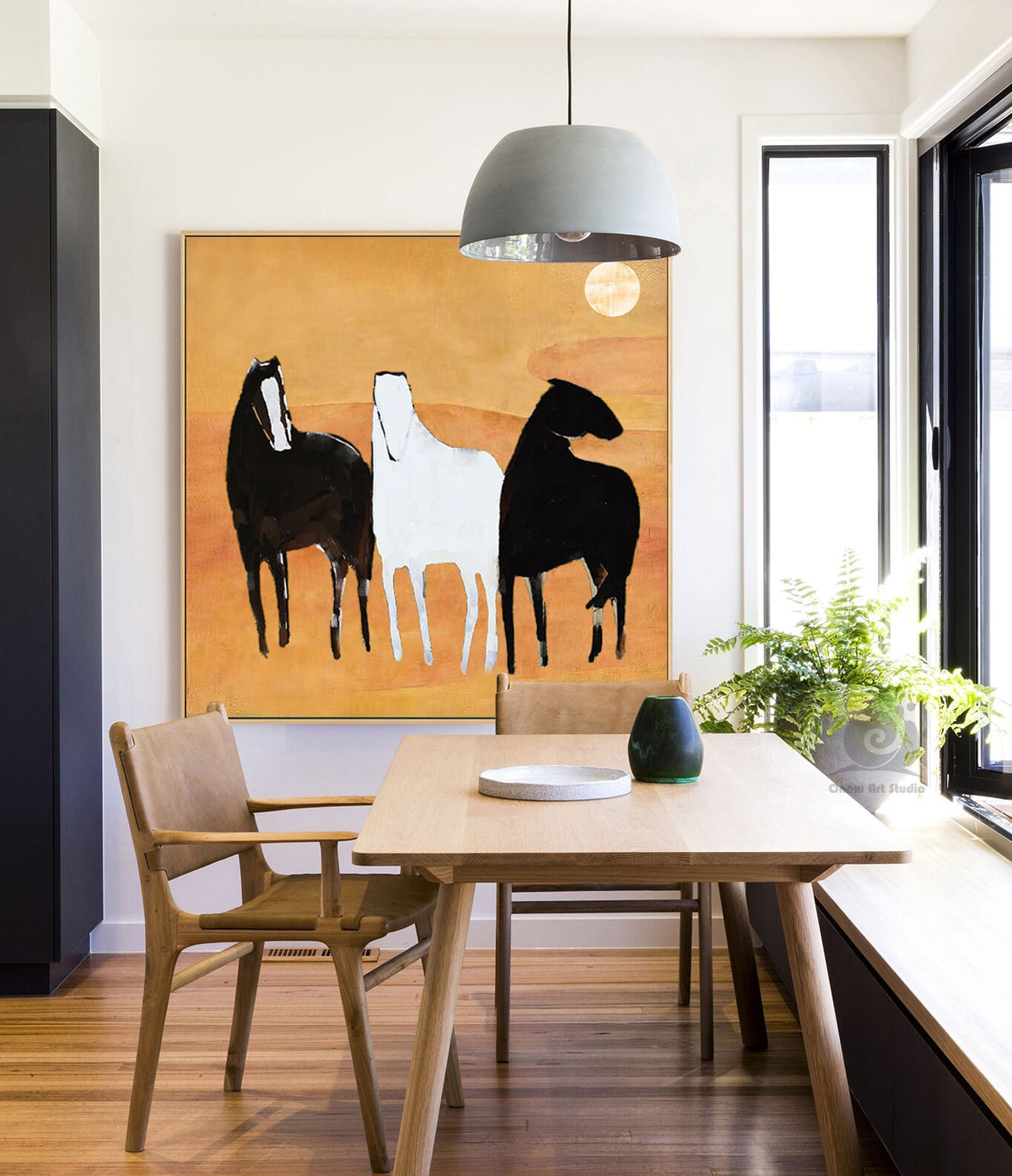 May include: Abstract painting of three horses in black, white, and gray against a yellow background. The painting is hanging on a wall in a dining room with a wooden table and chairs.