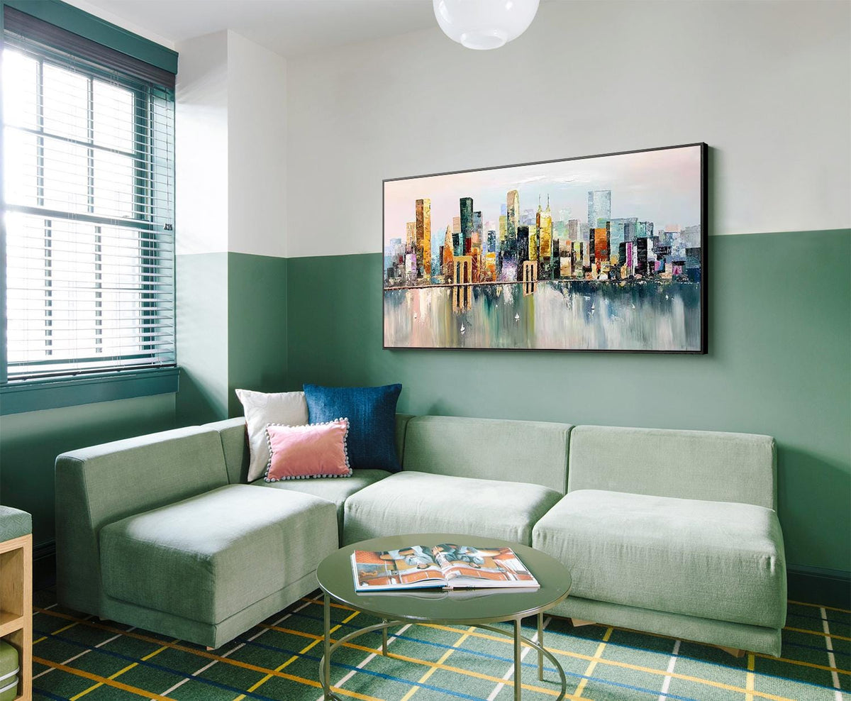 May include: A green sectional sofa with pink and blue throw pillows sits in front of a large painting of a city skyline. The painting is framed in black and hangs on a green wall. The sofa is in a room with a green and yellow checkered rug.