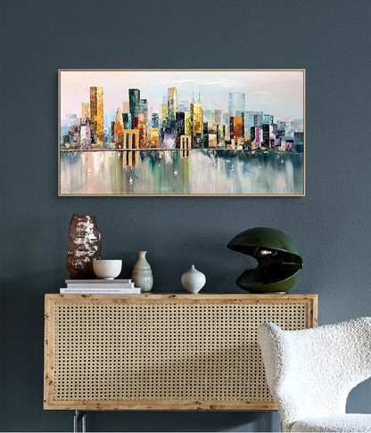 May include: A colorful abstract painting of a cityscape with buildings reflected in the water. The painting is framed in a light wood frame and is hanging on a dark blue wall.