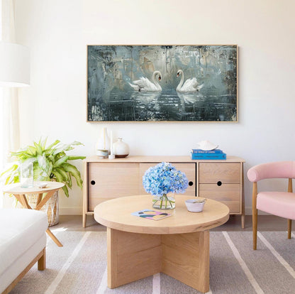 May include: A living room interior with a light wood coffee table, a light wood cabinet with two drawers, a pink armchair, a potted plant, and a framed painting of two white swans on a blue and gray background.