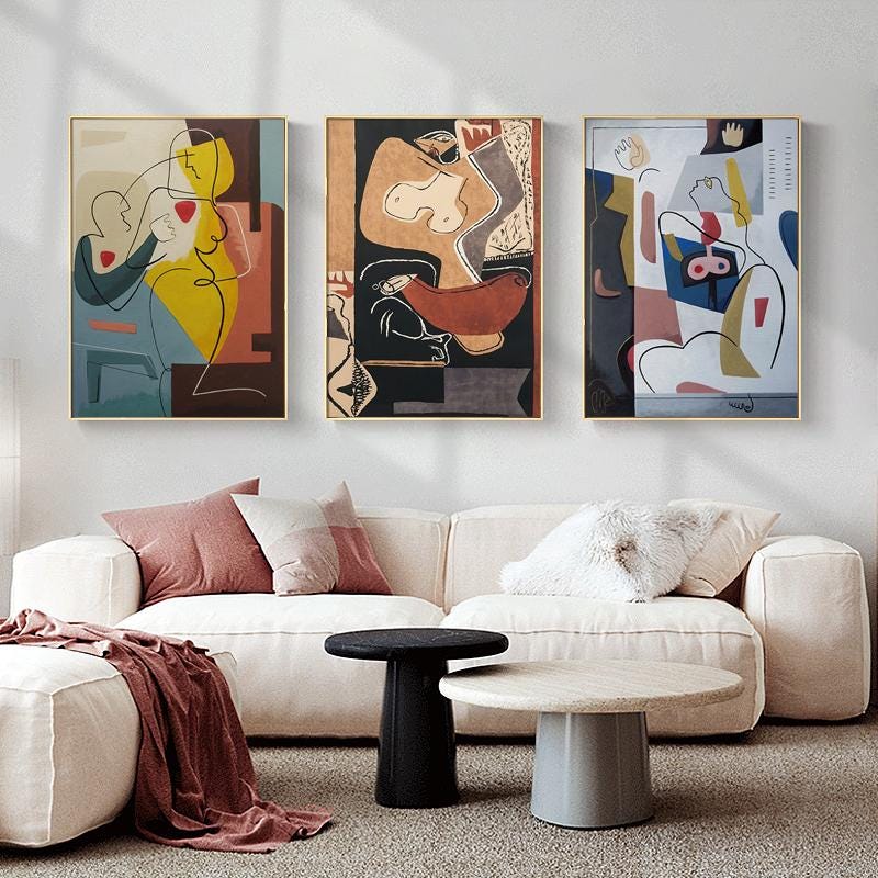 May include: Three abstract art prints featuring colorful geometric shapes and line drawings of figures. The prints are framed in gold and hung on a white wall above a white couch.