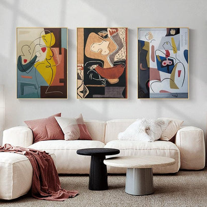 May include: Three abstract art prints featuring colorful geometric shapes and line drawings of figures. The prints are framed in gold and hung on a white wall above a white couch.