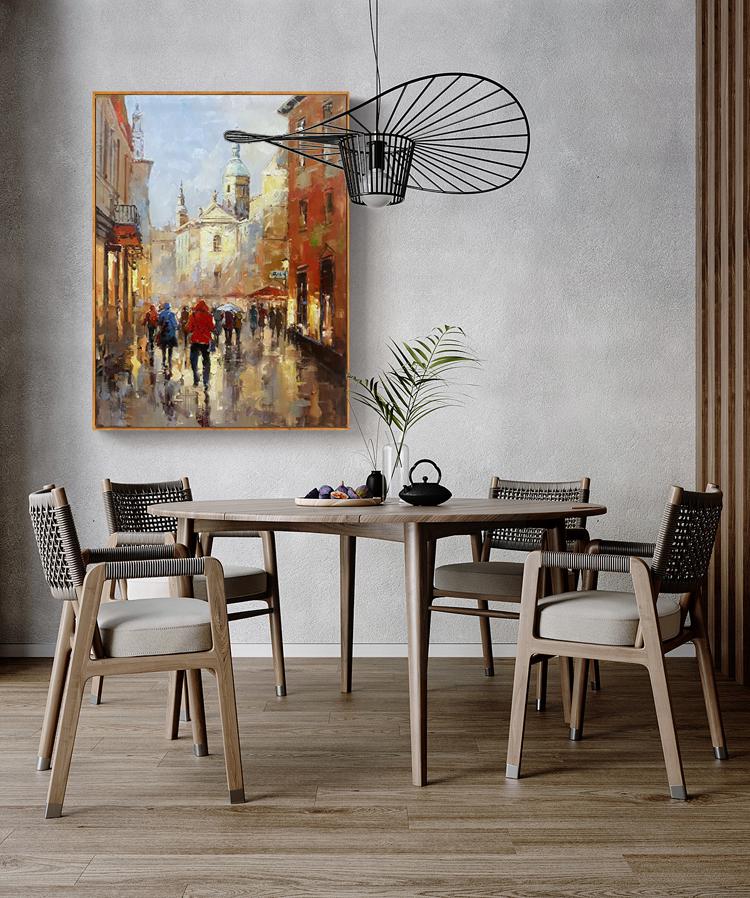 May include: A painting of a city street scene with people walking in the rain. The painting is framed and hanging on a wall above a wooden dining table with chairs.