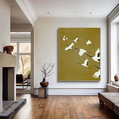 May include: A large rectangular wall art piece featuring a flock of white cranes with black wingtips and red crowns flying across a solid mustard yellow background. The birds are depicted in various positions of flight, creating a sense of movement.
