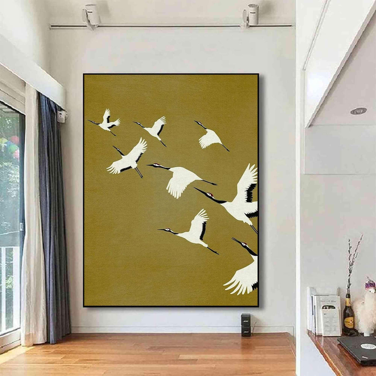 May include: A large rectangular wall art piece featuring a flock of white cranes with black wingtips and red crown markings flying across a solid mustard yellow background. The painting is framed in a thin black border and mounted on a white wall.