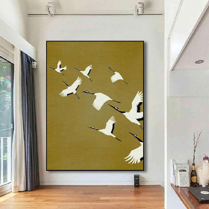 May include: A large rectangular wall art piece featuring a flock of white cranes with black wingtips and red crown markings flying across a solid mustard yellow background. The painting is framed in a thin black border and mounted on a white wall.