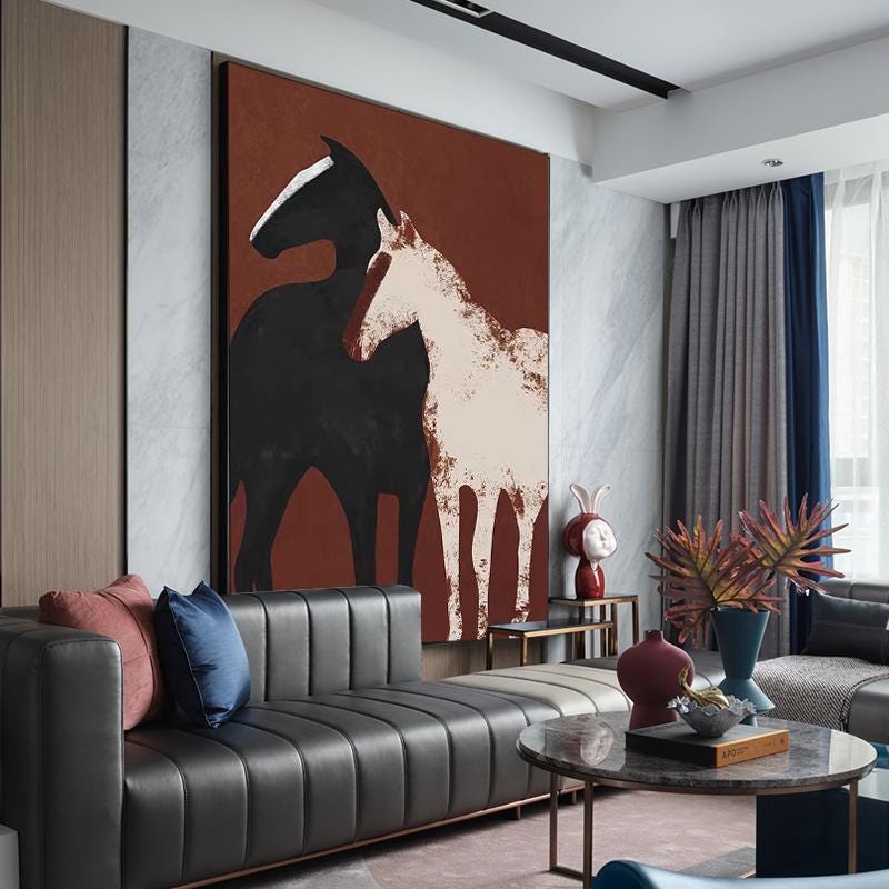 May include: Abstract painting of two horses, one black and one white, on a red background. The painting is hanging on a wall in a living room with a black leather sofa, a coffee table, and a vase with red flowers.