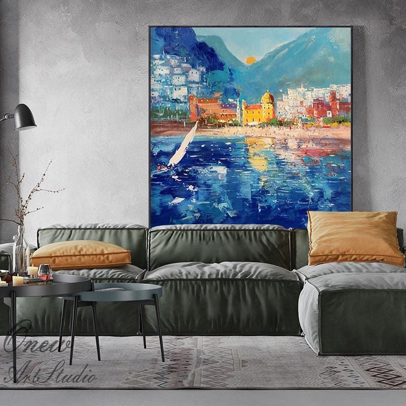 May include: A painting of a coastal town with a sailboat in the foreground. The town is built on a hillside with a mountain in the background. The water is blue and the sky is a bright blue with white clouds. The painting is done in a loose, impressionistic style.