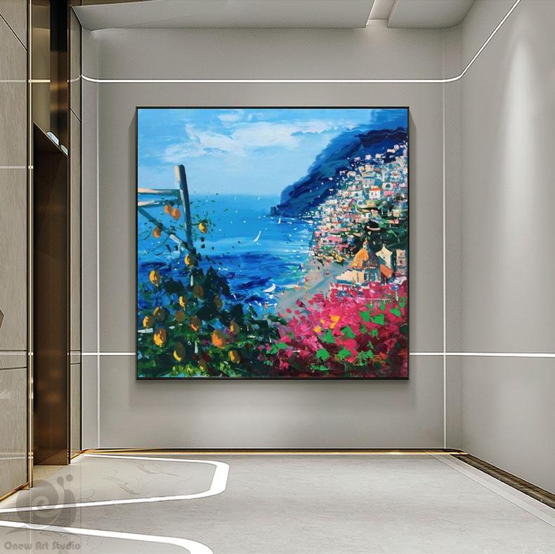 May include: A colorful painting of a coastal town with a blue sea and a lush green hillside. The painting features a vibrant mix of colors, including pink, yellow, and blue. The town is built on the hillside, with buildings cascading down to the water's edge. The painting is framed in a black frame.
