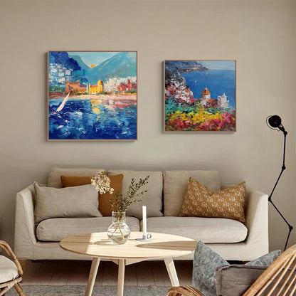 May include: Two colorful paintings of coastal scenes. The painting on the left shows a blue ocean with a sailboat and a town in the background. The painting on the right shows a town with colorful buildings and a blue ocean in the background.