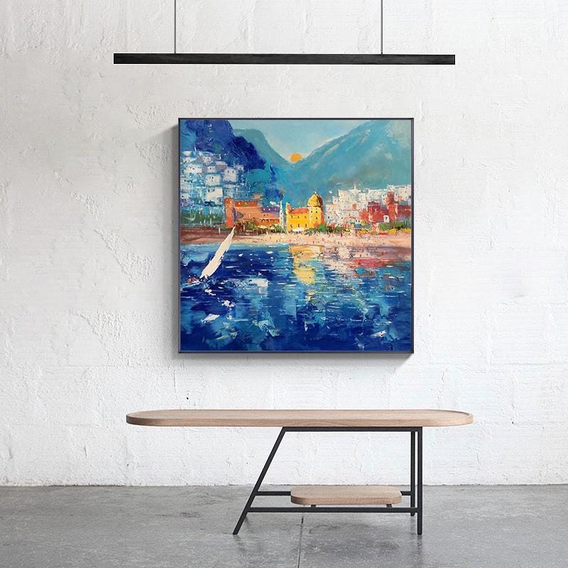 May include: A colorful painting of a seaside town with a sailboat in the foreground. The town is built on a hillside with a mountain in the background. The sky is blue with a bright sun setting in the distance.
