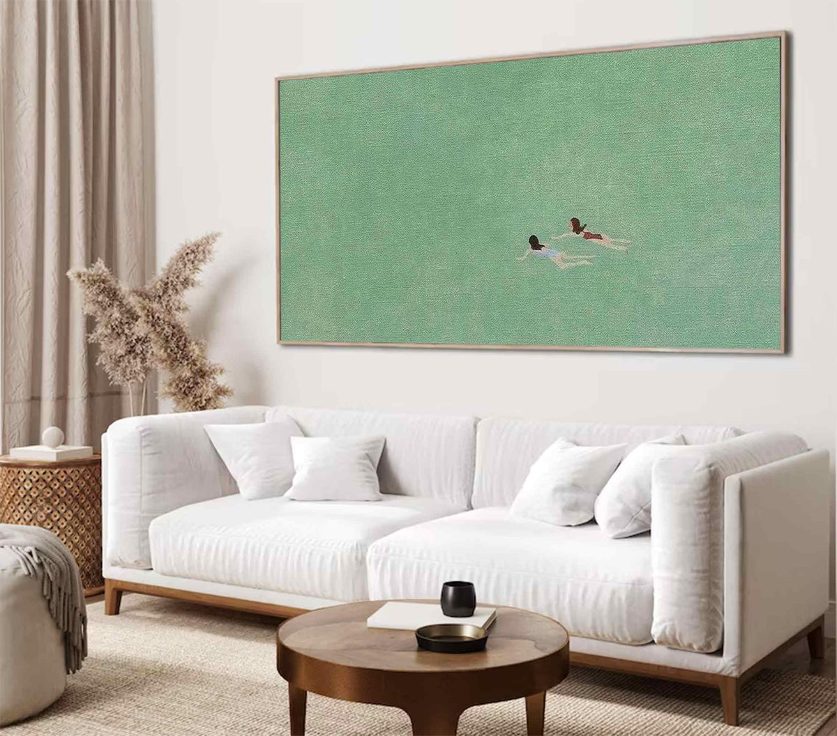 May include: A white sofa with two pillows sits in front of a large green canvas painting depicting two figures swimming in a body of water.