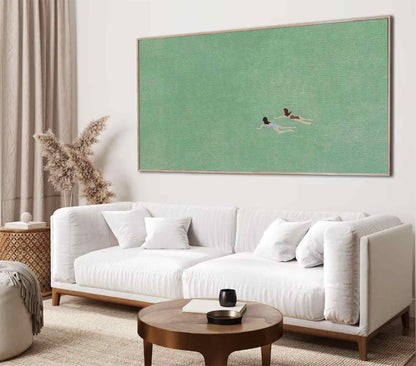 May include: A white sofa with two pillows sits in front of a large green canvas painting depicting two figures swimming in a body of water.