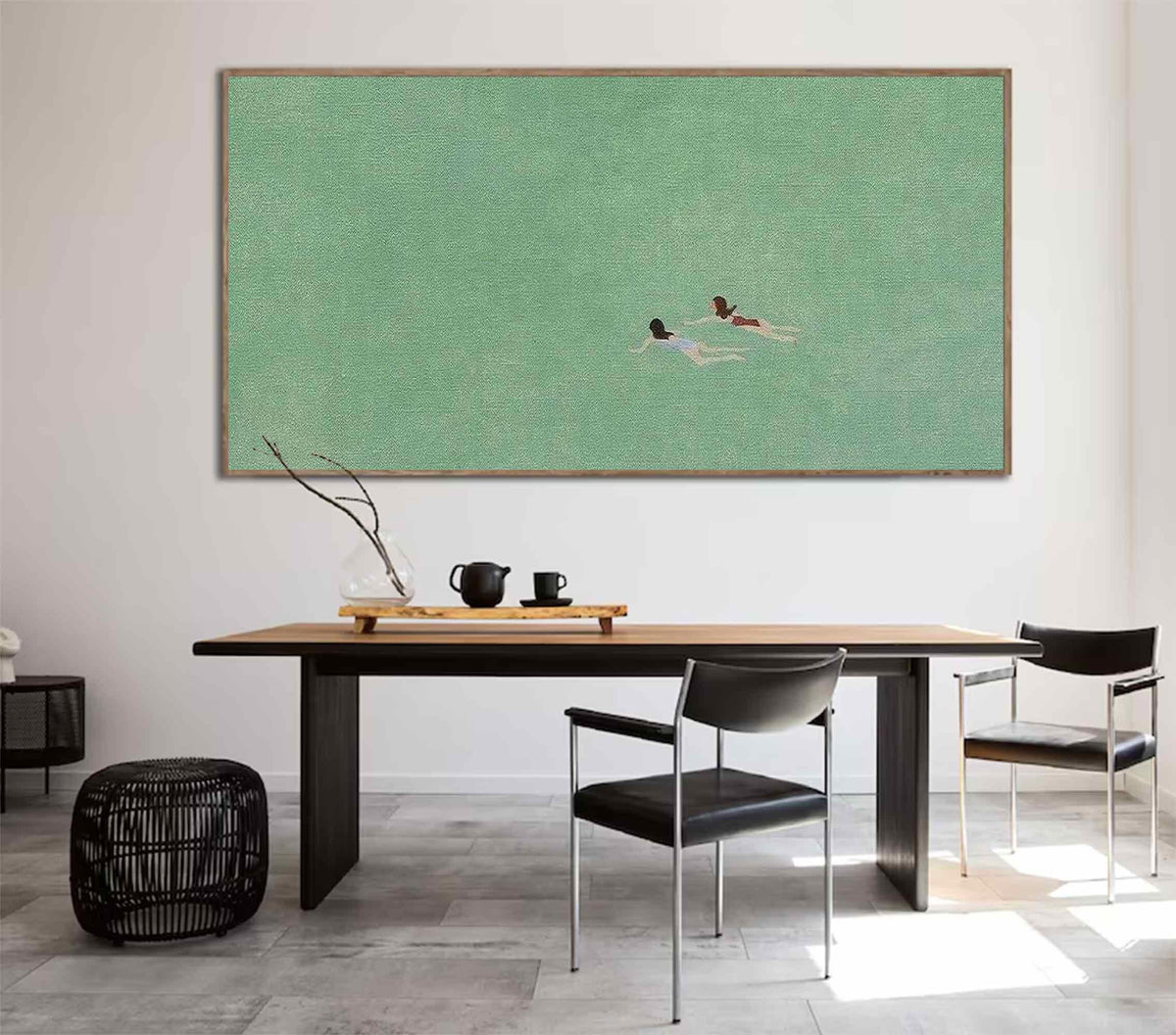 May include: A framed painting of two people swimming in a green body of water. The painting is hanging on a white wall above a wooden table with two black chairs.