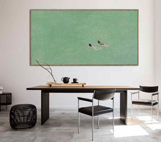 May include: A framed painting of two people swimming in a green body of water. The painting is hanging on a white wall above a wooden table with two black chairs.