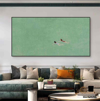 May include: A minimalist painting of two figures swimming in a green body of water. The painting is framed and hanging on a white wall above a couch with pillows.