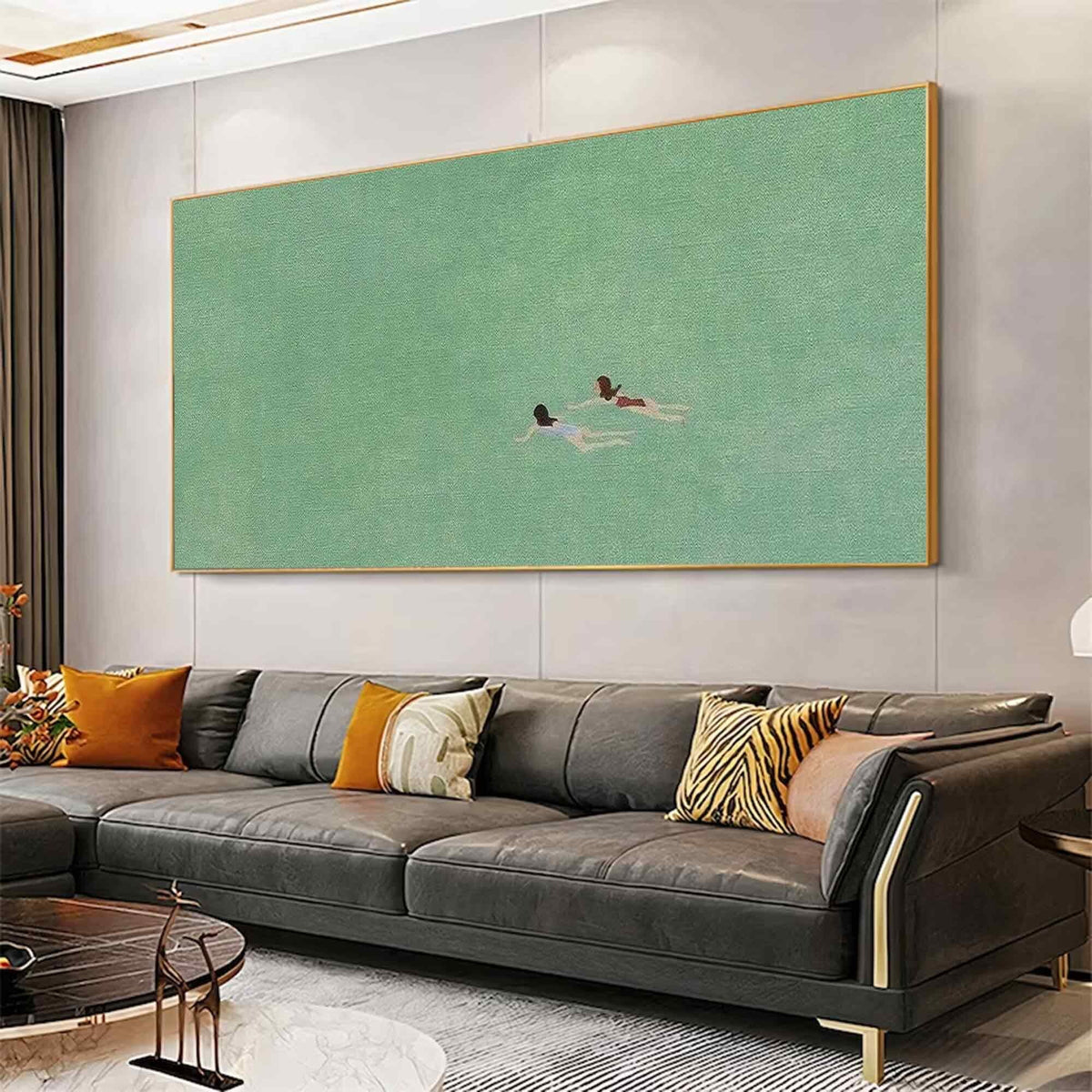 May include: A framed abstract painting with a green background and two figures swimming in the water. The painting is hanging on a wall above a gray leather sofa with pillows.