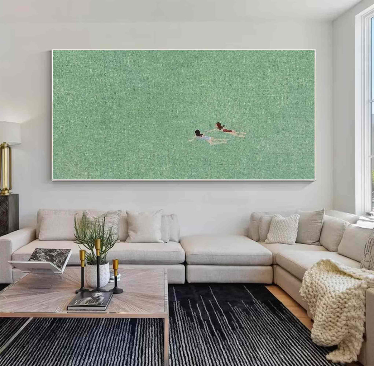 May include: A painting of two people swimming in a green body of water. The painting is framed and hanging on a white wall above a light gray sectional sofa.