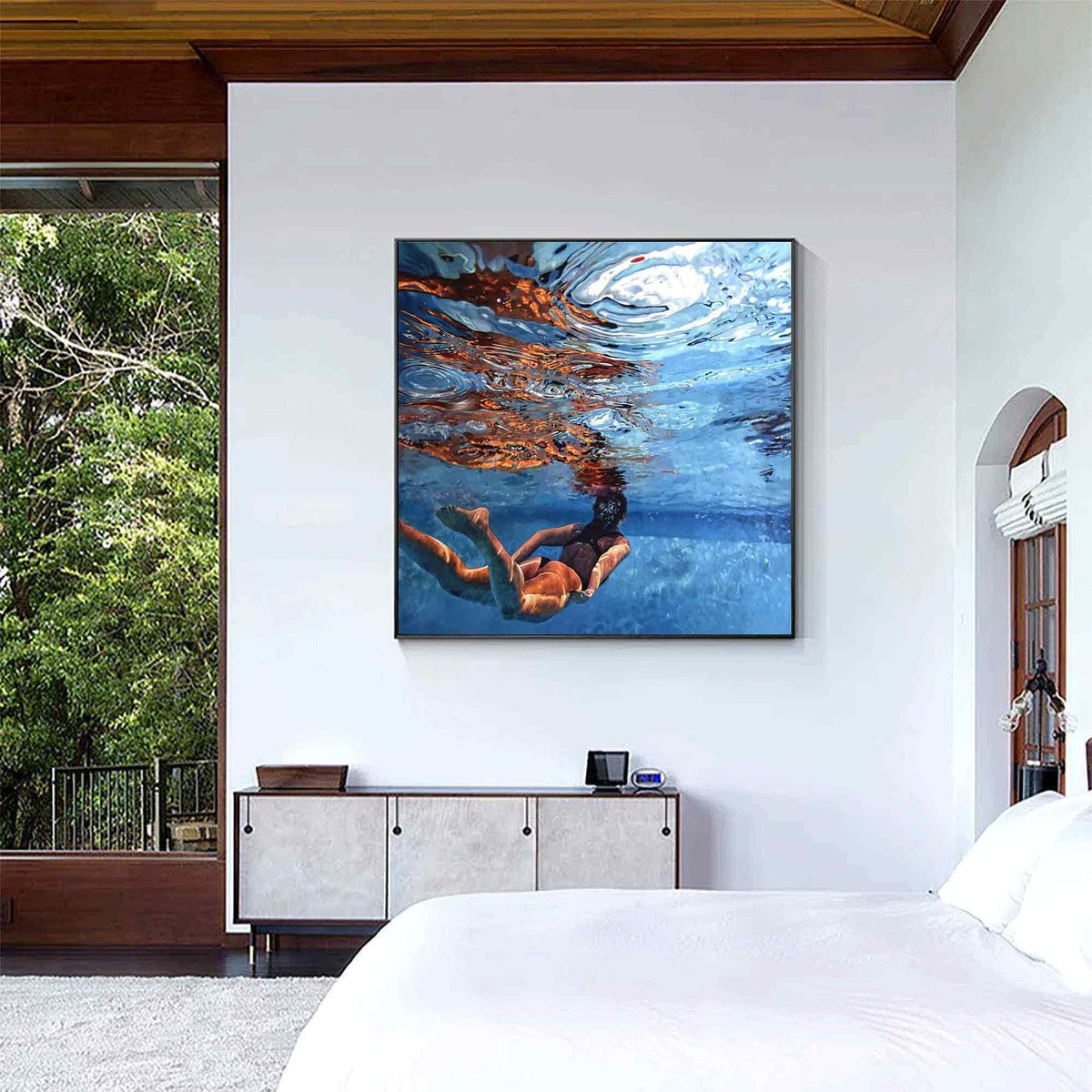 May include: A square wall art print featuring an underwater scene of a person swimming in a pool. The image captures the blue water, light reflections on the surface, and the swimmer's body submerged in the clear, bright, and deep blue water.