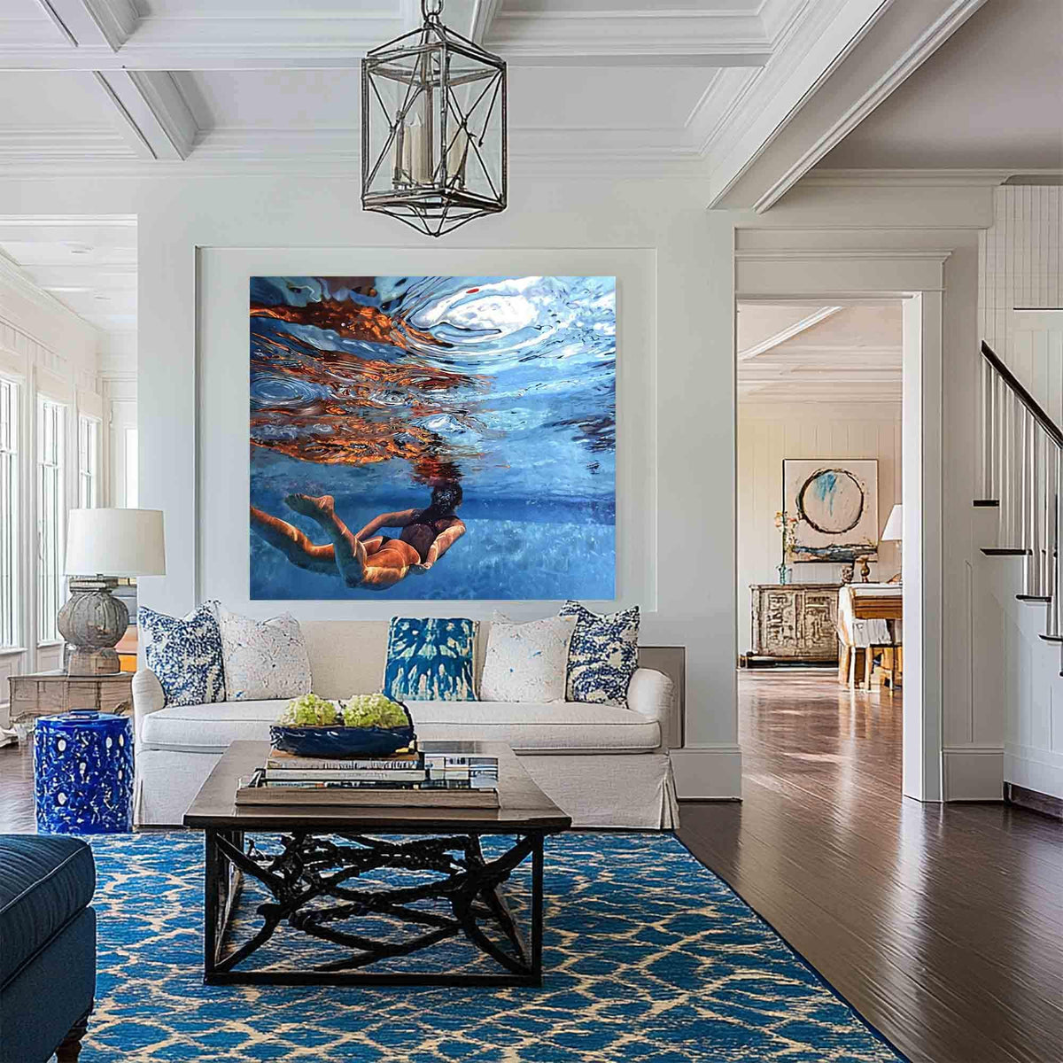 May include: A large square wall art print depicting an underwater scene of a person swimming in clear blue water. The image captures the light refraction on the surface and the swimmer's silhouette, displayed in a bright, modern living room setting.