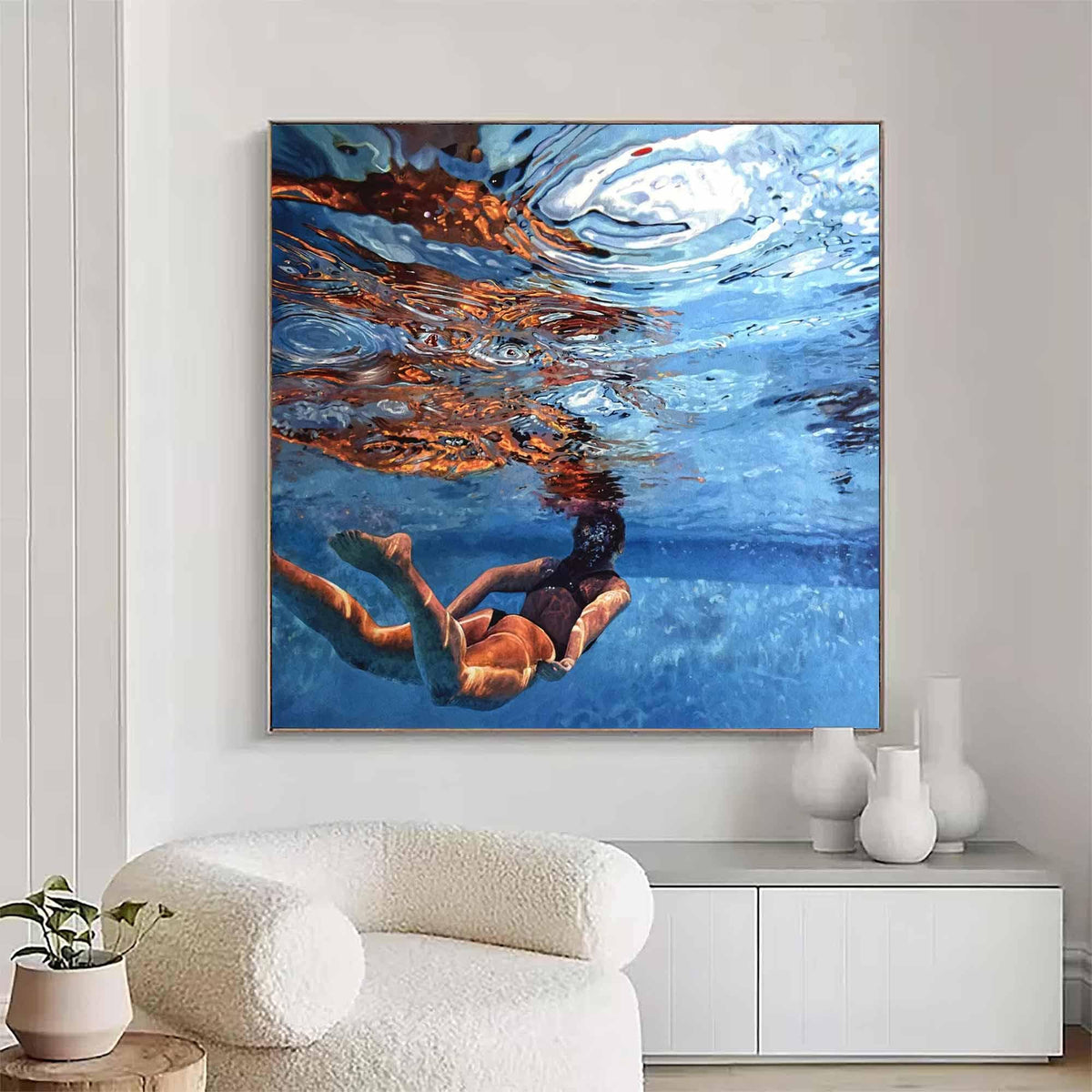 May include: A square wall art print depicting an underwater scene with a person swimming in clear blue water. The surface of the water shows light reflections and ripples in shades of orange and white, while the depths are a deep blue.