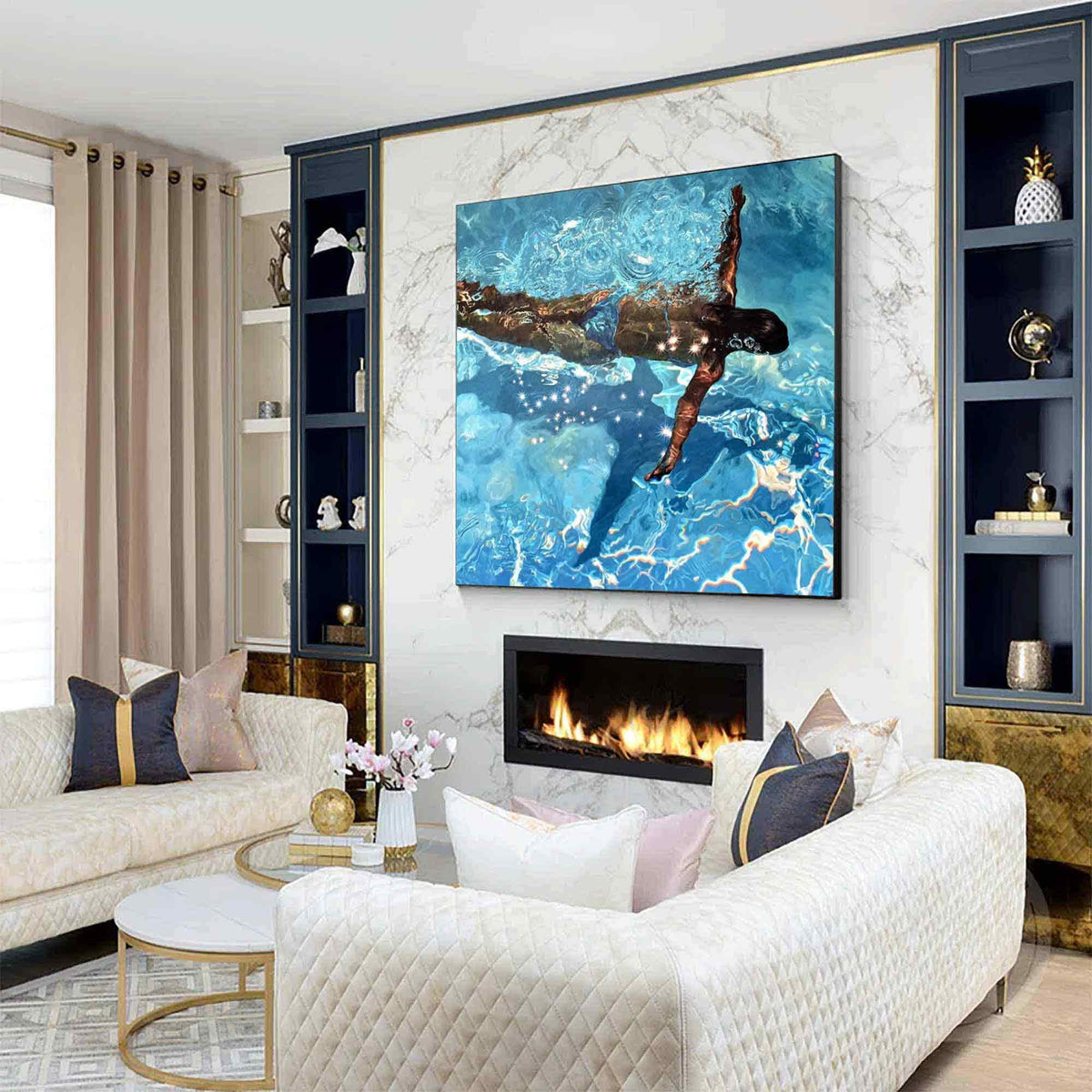 May include: A living room with a large square painting of a person swimming in a pool. The painting is above a fireplace with a black frame. The room has a white quilted sofa, a round coffee table, and built-in shelves.