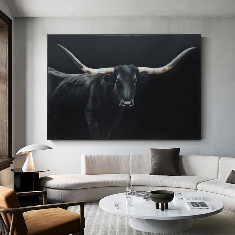 May include: A large, framed canvas art piece featuring a black longhorn bull against a dark background. The bull's horns are a light beige color, and the artwork is displayed above a white sofa in a modern living room setting.