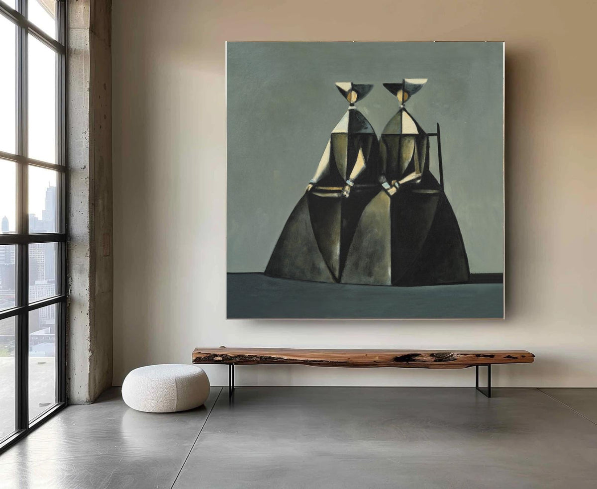 May include: An abstract painting features two figures in dark dresses and hats against a muted green background. The artwork is framed and hangs above a wooden bench with black metal legs. A white, round ottoman sits on the polished concrete floor.