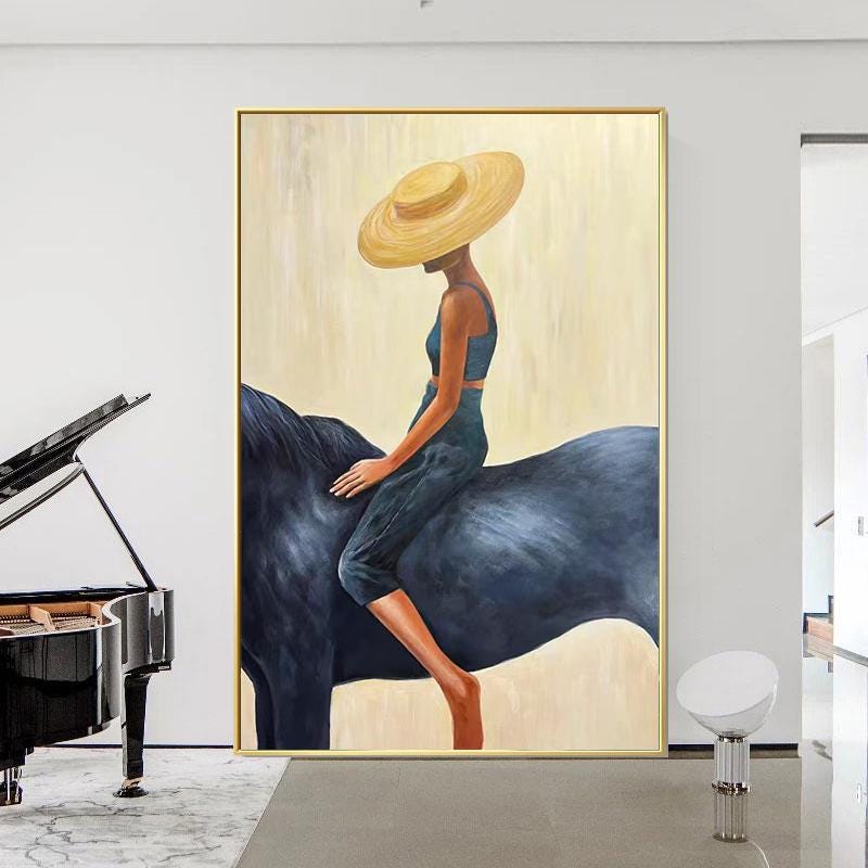 May include: An abstract painting depicts a figure wearing a wide-brimmed yellow hat and dark blue clothing, riding a dark blue horse. The artwork is framed in gold and set against a cream-colored background.