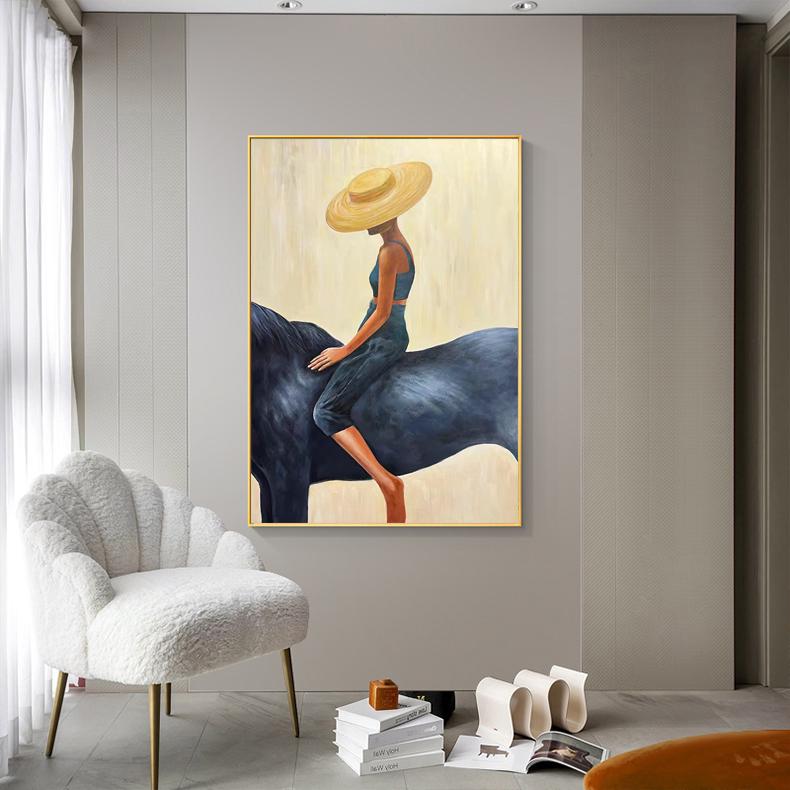 May include: An abstract painting depicts a person riding a dark blue horse. The person wears a yellow hat, a blue top, and dark blue pants. The artwork is framed in gold and hangs on a neutral-colored wall.