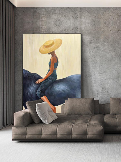 May include: An abstract painting depicts a person wearing a wide-brimmed straw hat and a blue outfit, seated on a dark blue form. The artwork is framed and displayed above a brown sectional sofa with gray pillows, set against a gray wall.
