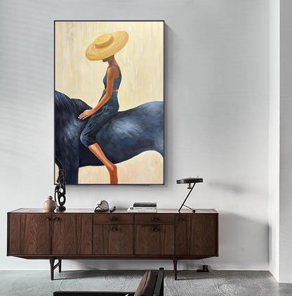 May include: An abstract painting depicts a person riding a dark blue horse. The person wears a yellow hat, a blue top, and blue pants. The background is a light beige color, and the painting is framed in black.