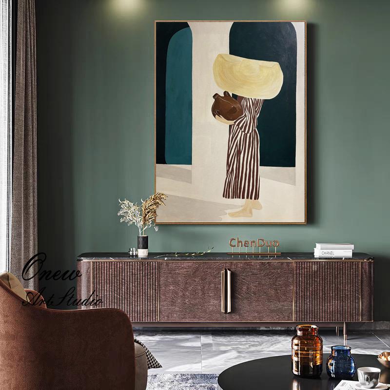 May include: An abstract painting depicts a figure carrying a large, yellow object and a brown vessel. The figure is dressed in a striped dress. The artwork is framed and hangs on a green wall. The painting is part of a home decor setting.