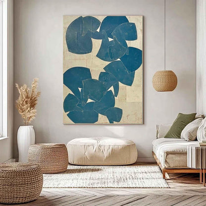 May include: Abstract wall art featuring a large canvas with a cream-colored background and overlapping blue shapes. The artwork is displayed in a living room setting with woven ottomans, a beige ottoman, and a sofa with green pillows.