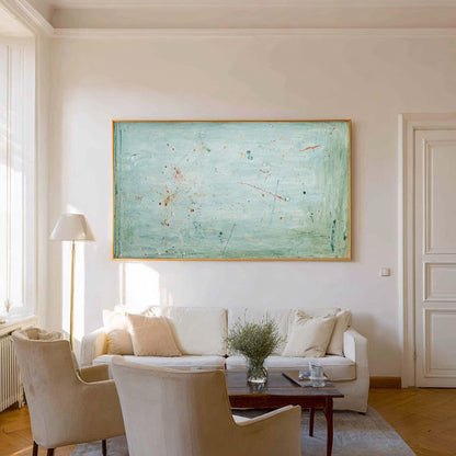 May include: An abstract painting with a light blue background and a wooden frame. The artwork features splashes of red, orange, and blue paint. The painting hangs above a white sofa with beige chairs and a wooden coffee table.